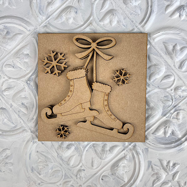 Introducing the Winter Interchangeable Squares by Janet's Craft Corner: a charming decorative wooden plaque designed for tiered trays. It features a cutout design of two ice skates hanging with a bow, surrounded by three snowflakes, and set against a textured white background. This piece is perfect for adding charm to your seasonal décor.