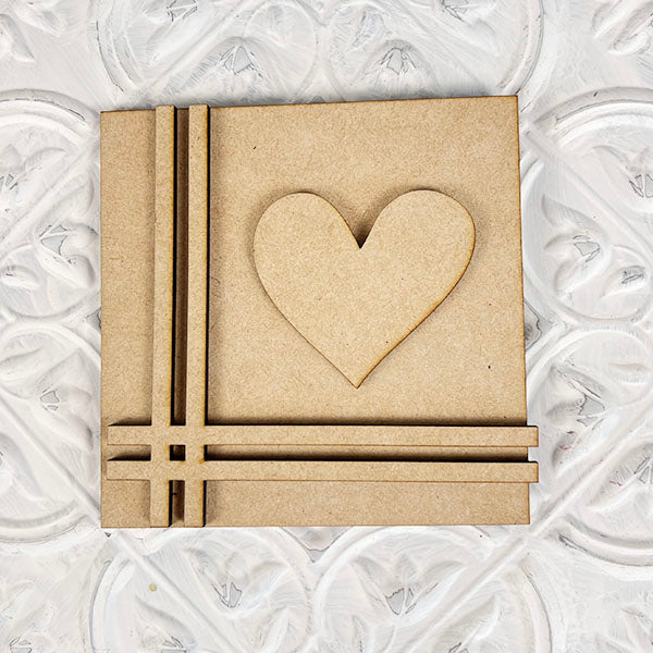 The Home Family Interchangeable Square by Janet's Craft Corner is a delightful decorative wooden panel ideal for home decor. It showcases a raised heart design on the right side, complemented by vertical and horizontal grooves on the left, all set against a textured white surface with swirling patterns.