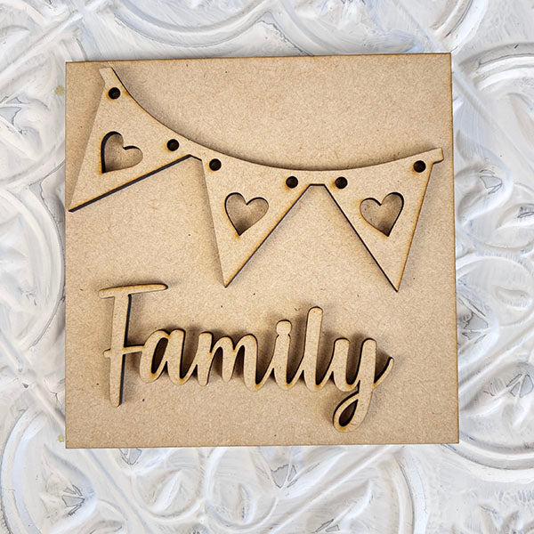 Discover the "Home Family Interchangeable Squares" by Janet's Craft Corner, featuring a charming wooden sign adorned with heart-shaped cutouts and the word "Family" in an elegant cursive font. The textured, ornate white background enhances its appeal, making it a perfect addition to your home decor. This mini sign adds warmth and can effortlessly integrate with other interchangeable signs for any season.