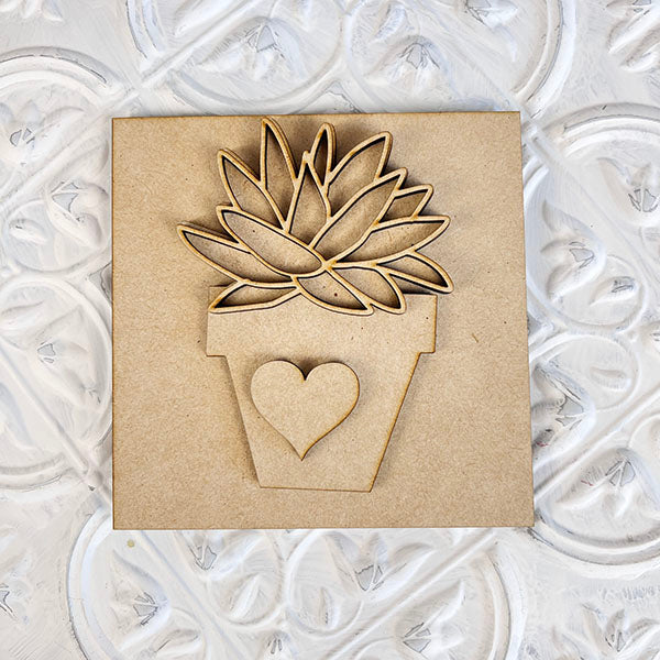 Janet's Craft Corner's Home Family Interchangeable Squares features a charming decorative cutout mini sign, showcasing a potted succulent with a heart on the pot, set against a textured white background to enhance your home decor.