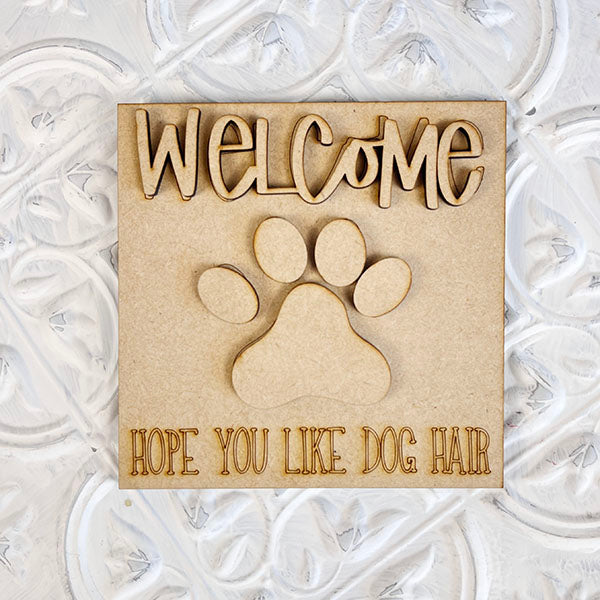 The "Dog Interchangeable Squares" from Janet's Craft Corner adds a delightful touch to your decor with its charming wooden design. It adorns the decorative white wall with a cutout paw print, embracing rustic farmhouse elements. The top warmly greets visitors with "Welcome," while the bottom playfully notes, "Hope you like dog hair," providing a delightful canine element to your space.