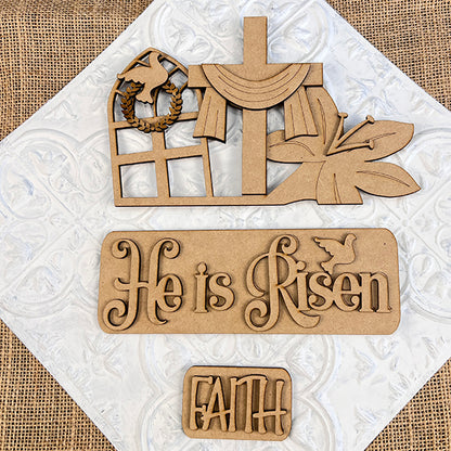 Janet's Craft Corner offers the "He is Risen Interchangeable Insert" DIY home decor kit, which showcases wooden cutouts of a draped cross, a butterfly, and a window featuring a dove and wreath. The kit includes two plaques with the messages "He is Risen" and "Faith," designed to be interchangeable on a textured white and burlap background for an Easter-themed craft experience.