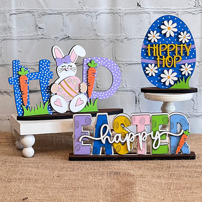 Discover Janet's Craft Corner's "Easter Trio Mini Shelf Sitters," which includes a wooden display featuring "HOP" complete with a bunny and carrots, an egg adorned with "HIPPITY HOP," and vibrant letters spelling out "EASTER happy." Ideal for a DIY kit project, these delightful shelf sitters are beautifully presented on burlap set against a white brick backdrop.