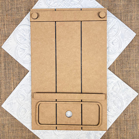 The Pallet Interchangeable Base, part of the DIY home decor kit by Janet's Craft Corner, features a blank brown surface with two clips and a circular hole at the bottom center. It is artfully positioned on a decorative, textured background, adding a charming touch to your home décor. The board is sectioned off with black lines on its wood or cardboard surface for added versatility.