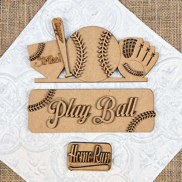 Introducing Janet's Craft Corner's Baseball Interchangeable Insert, a DIY home decor kit featuring laser-cut wooden decorations with baseball-themed designs such as a cap, bat, ball, and glove. This kit includes texts like "Strike," "Play Ball," and "Home Run," all set against a textured background for the ultimate crafting experience.