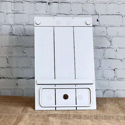 The Pallet Interchangeable Base - Painted by Janet's Craft Corner, a testament to expert craftsmanship, is displayed against a white brick wall atop a beige fabric surface. Its minimalist design includes a rectangular cutout at the bottom center, offering an elegant addition to any home decor.