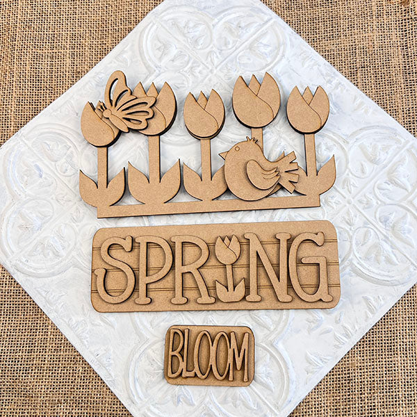 The Spring Tulips Interchangeable Insert from Janet's Craft Corner is a delightful DIY home decor kit that includes hand-painted wooden cutouts with a floral and spring theme. Featuring tulips, a butterfly, a bird, and the words "SPRING" with a tulip in place of the letter "I" and "BLOOM," this craft kit allows you to easily update your seasonal display.