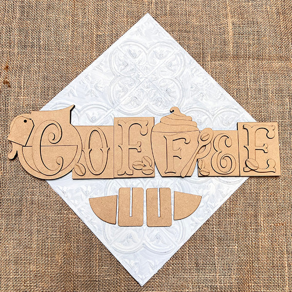 The Coffee Word Block DIY kit by Janet's Craft Corner spells "COFFEE" with a cup and jar motif on white textured tile and burlap, plus extra wooden shapes—perfect seasonal home decor for coffee lovers. Set of 1.