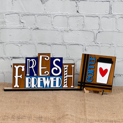 Janet's Craft Corner's Coffee Squares feature charming wooden signs on burlap with "FRESH BREWED" and "COFFEE" (cup and red heart) designs, perfect for DIY seasonal home decor in small spaces against a white brick wall.