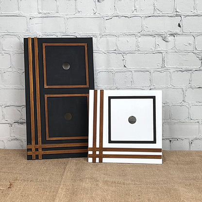 Janet's Craft Corner presents the Farmhouse Trim Interchangeable Squares Holder, featuring two decorative square frames displayed against a white brick wall. The larger frame boasts a black finish with striking brown and gold striped accents, and the smaller frame is elegantly white with matching striped details. Both frames feature central circular cutouts that beautifully capture a farmhouse charm reminiscent of a DIY kit.