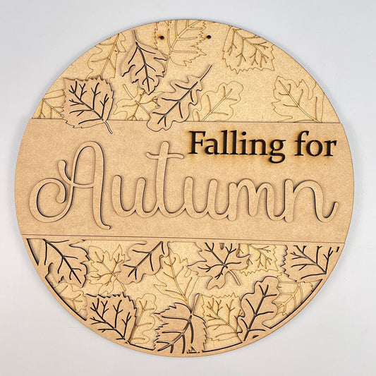 The Falling for Autumn Round DIY Home Decor Kit from Janet's Craft Corner features a round wooden plaque engraved with "Falling for Autumn" and beautifully carved leaf patterns, making it a delightful addition to your personalized fall-themed home décor.