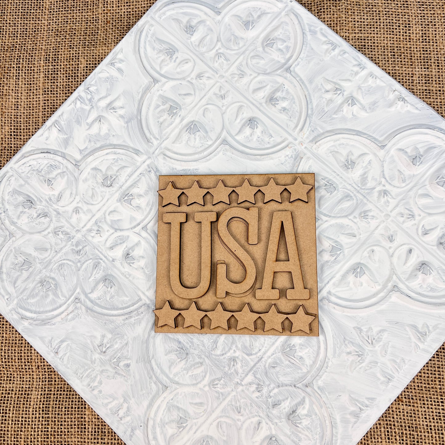 Introducing the Patriotic Interchangeable Squares from Janet's Craft Corner: a wooden sign featuring the letters "USA" encircled by stars, ideal for infusing your farmhouse décor with seasonal charm. The design is set on a textured white and burlap background, capturing a delightful mix of rustic elegance and patriotic spirit.