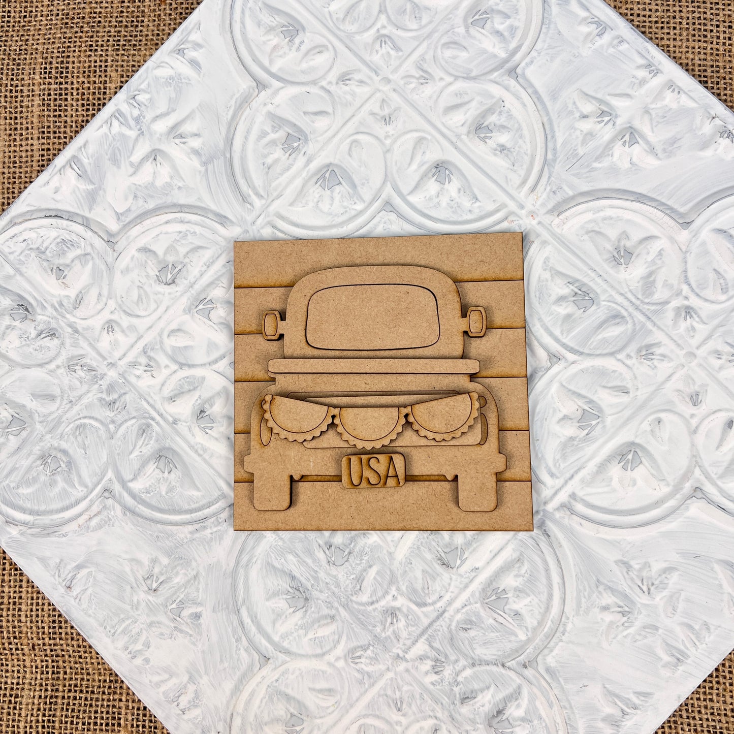 Introducing the "Patriotic Interchangeable Squares" by Janet's Craft Corner – a decorative wooden cutout featuring a pickup truck adorned with farmhouse décor. Its unique tailgate design showcases gears and the word "USA," perfect for adding seasonal charm against a textured white background with a patterned touch.