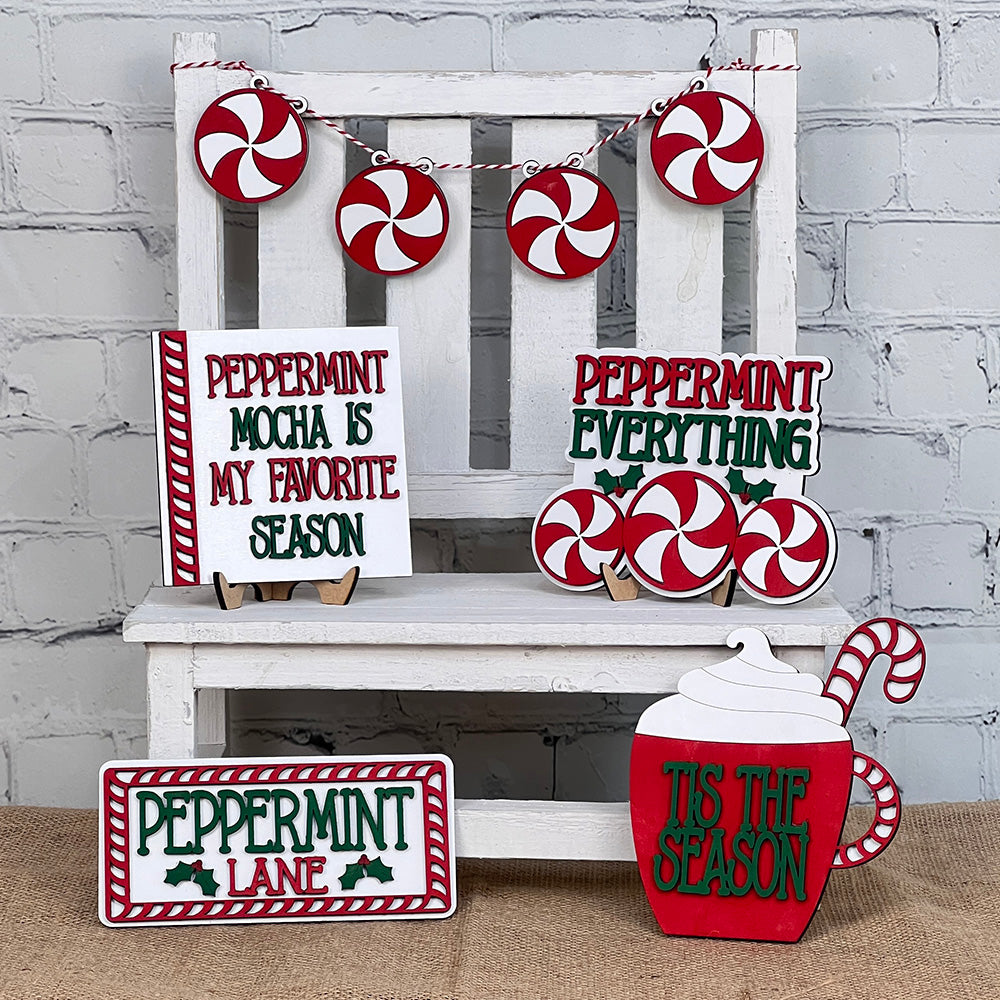 A festive arrangement featuring Janet's Craft Corner's Peppermint Mocha Tiered Tray DIY Home Decor Kit adorns your space with peppermint-themed decorations. Charming signs reading “Peppermint Mocha is My Favorite Season,” “Peppermint Everything,” and a warm greeting to “Peppermint Lane” highlight the display. The delightful red and white peppermint motifs are skillfully arranged throughout, bringing a cheerful ambiance perfect for your home décor.