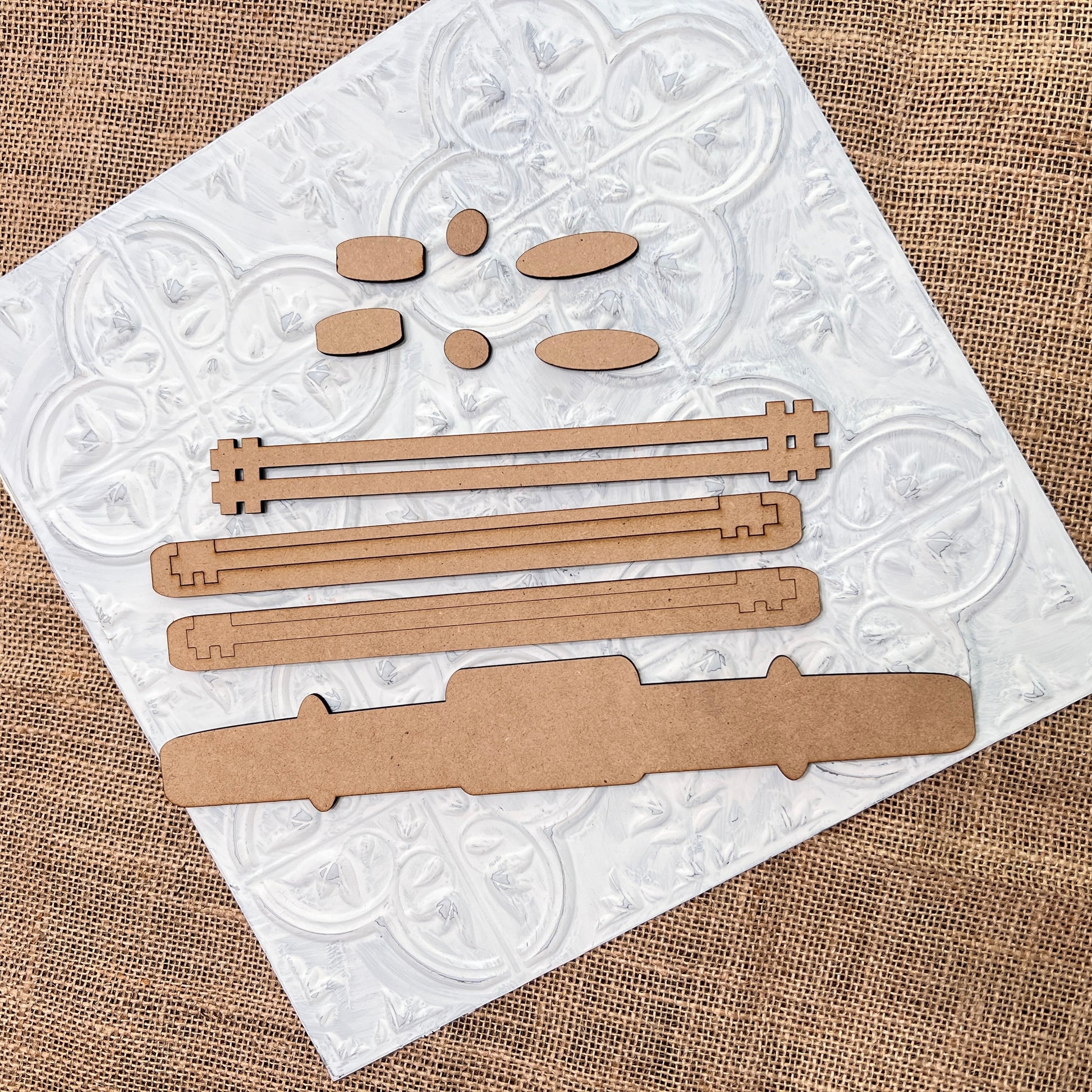 Janet's Craft Corner's Antique Truck Base Double-Sided Add-On DIY craft kit set is arranged on a textured white tile over burlap, perfect for creating or customizing truck-themed accessories.