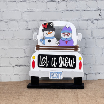 Janet's Craft Corner offers the "Let It Snow" DIY seasonal decor kit featuring an interchangeable insert with a pickup truck and snowman couple. The truck says "Let it snow" and has a "FROSTY" plate, adding winter cheer against its brick wall backdrop.