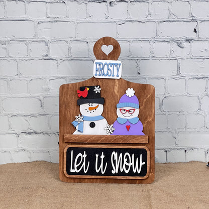 Janet's Craft Corner Let It Snow Interchangeable Insert is a DIY craft kit with 3 wooden pieces featuring a snowman couple, "FROSTY" sign, and "Let it snow" plaque—perfect for seasonal home decor.