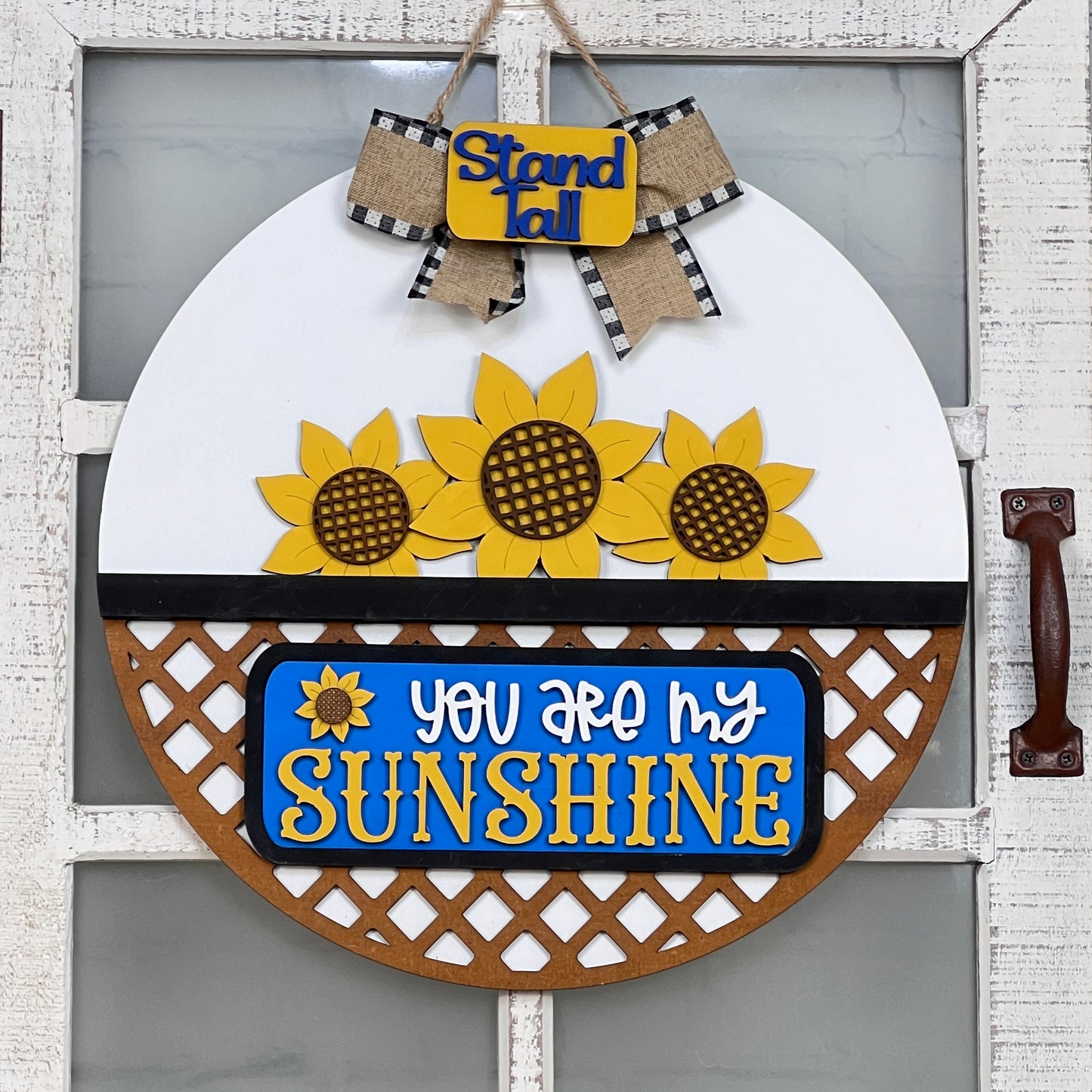 The Sunflower Interchangeable Insert by Janet's Craft Corner features a vibrant design with three sunflowers, "Stand Tall" at the top, and "You are my Sunshine" in bold on blue. Its circular layout with a lattice pattern offers charming DIY home decor.