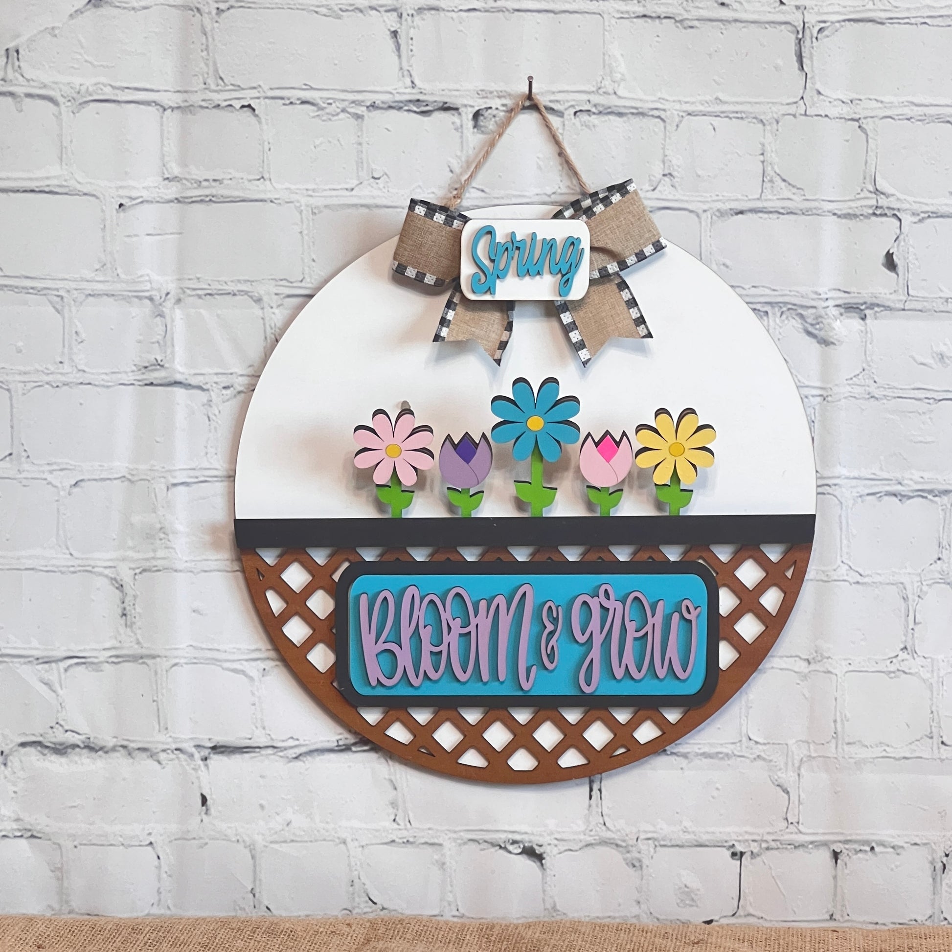 Janet's Craft Corner offers the Bloom & Grow Interchangeable Insert, a DIY decor kit featuring a Spring-themed round wall piece with Spring Blooms in a planter, "Spring" on a checkered ribbon, and "Bloom & Grow" in blue and pink hues reflecting an antique truck's charm.