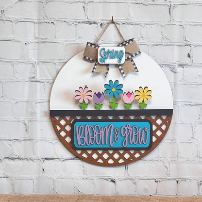 Janet's Craft Corner offers the Bloom & Grow Interchangeable Insert, a DIY decor kit featuring a Spring-themed round wall piece with Spring Blooms in a planter, "Spring" on a checkered ribbon, and "Bloom & Grow" in blue and pink hues reflecting an antique truck's charm.