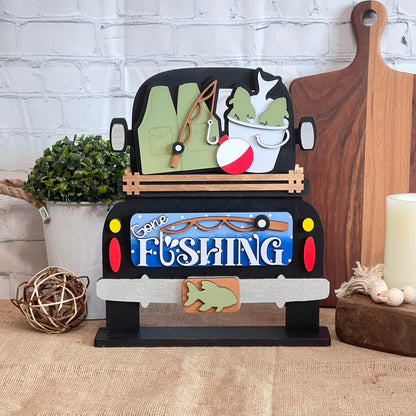 The Gone Fishing Interchangeable Insert by Janet's Craft Corner features a truck with fishing gear, fish bucket, and bobber—perfect for your DIY seasonal home decor craft kit (1 set of 3 pieces) as a charming decorative accent.