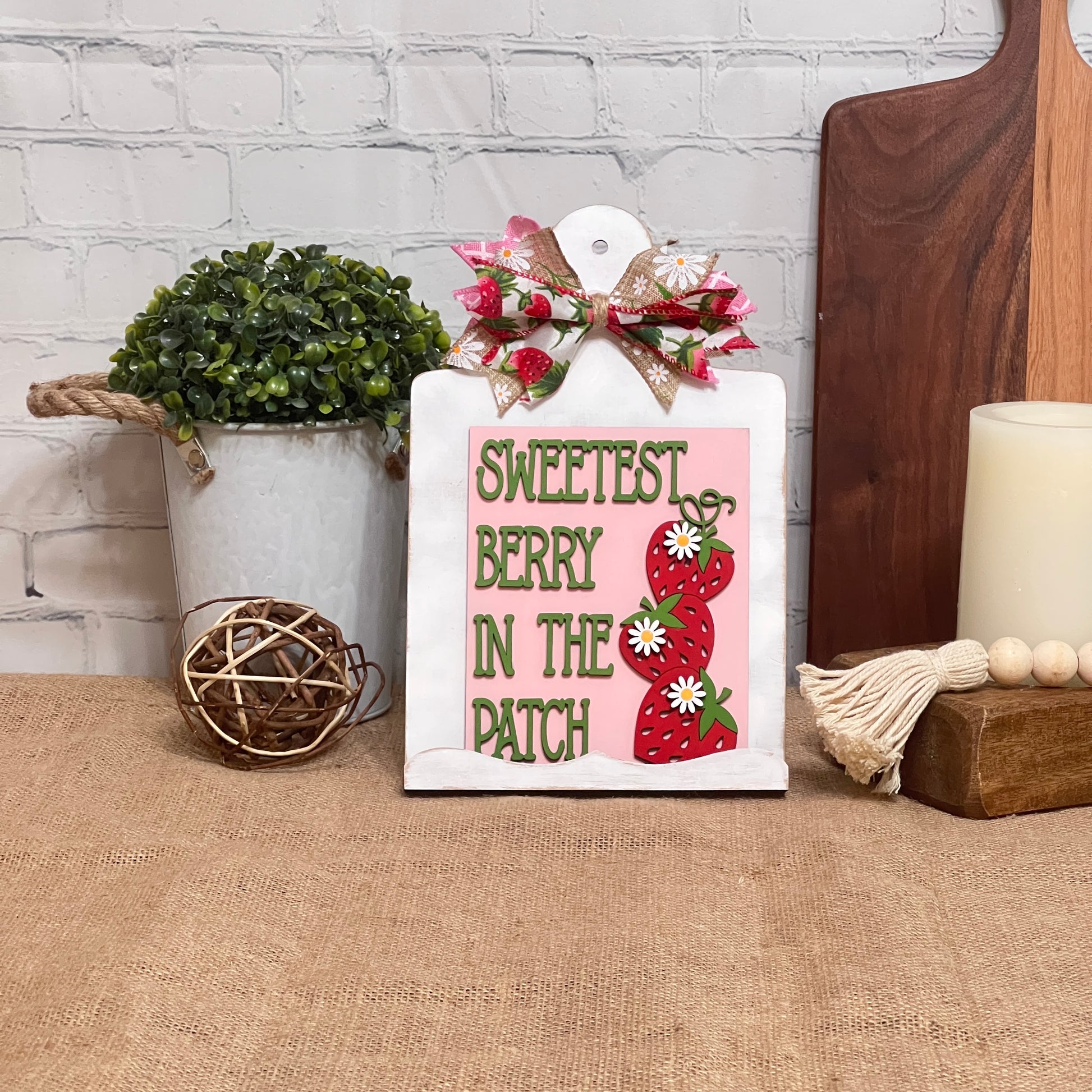 The "Berry Sweet Switchable Farmhouse Signs" DIY Craft Kit by Janet's Craft Corner features a sign with "Sweetest Berry in the Patch," strawberries, daisies, and a bow—perfect summer décor to display with plants, a candle, and more. Choose from 3 designs!.