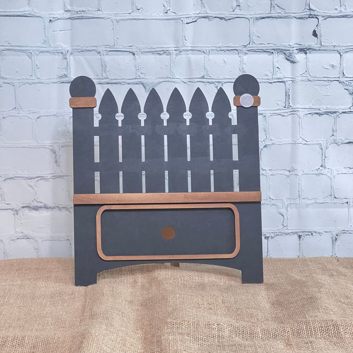 The Garden Fence Interchangeable Base - Painted by Janet's Craft Corner is a small decorative wooden shelf with a picket fence design, gray paint, brown trim, and a bottom drawer—perfect for DIY decor.