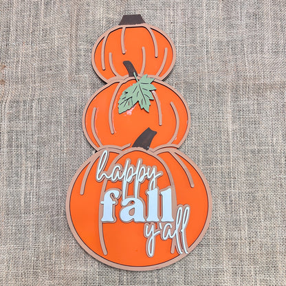 The Reversible Snowman/Pumpkin Shelf Leaner by Janet's Craft Corner is a DIY seasonal home decor kit featuring three stacked orange pumpkins on burlap; the bottom pumpkin reads "happy fall y'all," and a green leaf accents the center.