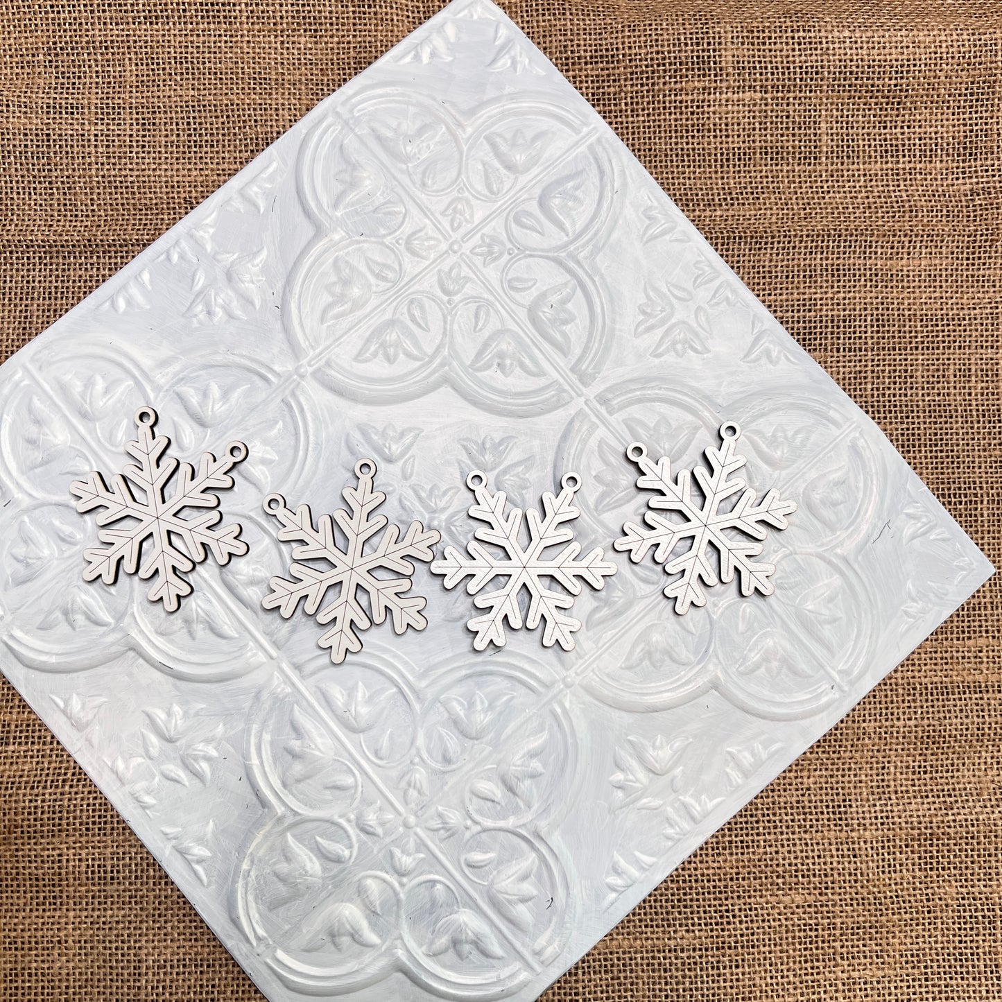 Four Tiered Tray Garlands from Janet's Craft Corner are arranged in a row on a white decorative tile set atop burlap fabric.