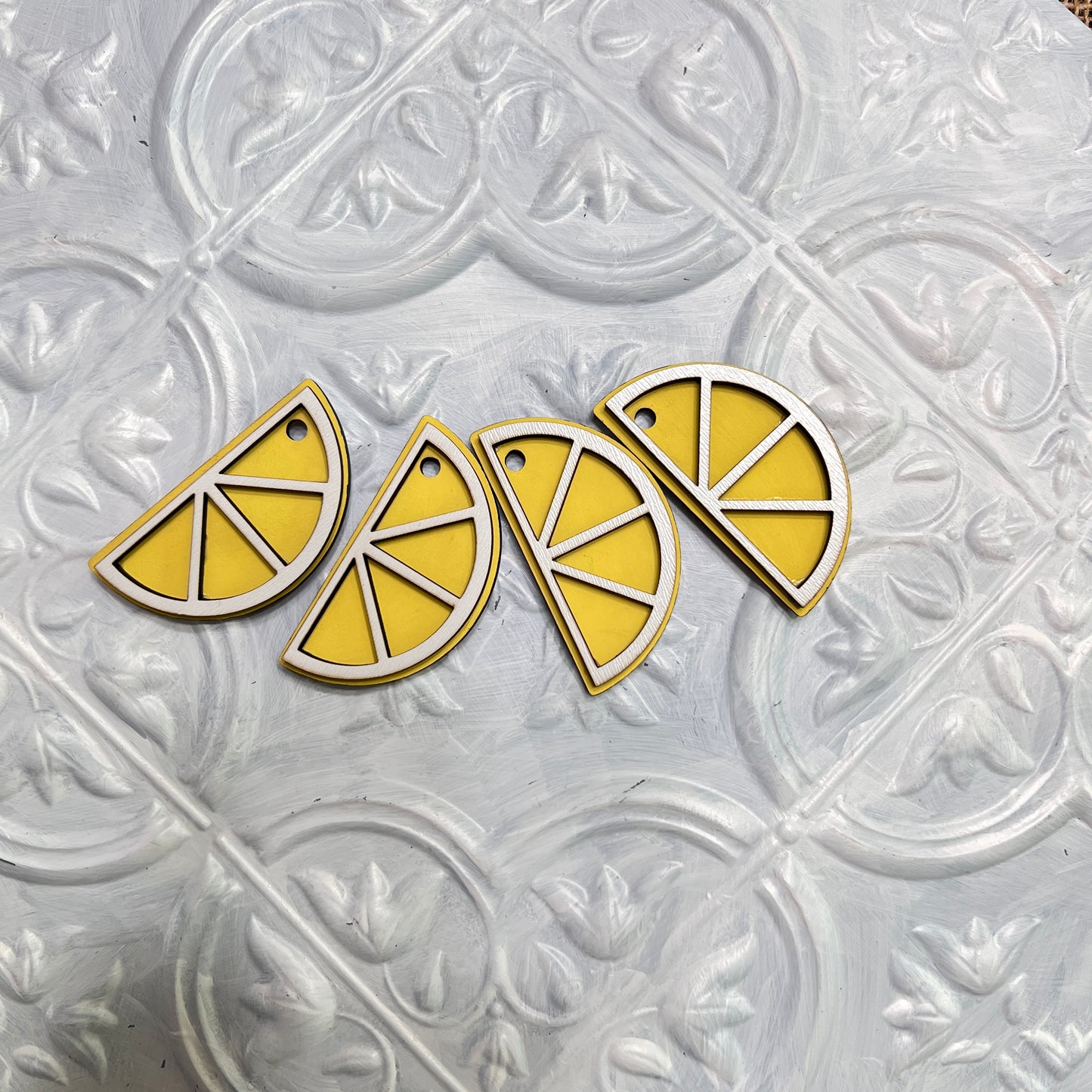 Four yellow and white lemon slice-shaped charms from Heartland’s Tiered Tray Garlands - Painted (Choice of 12) are lined up on an ornate, textured white surface.