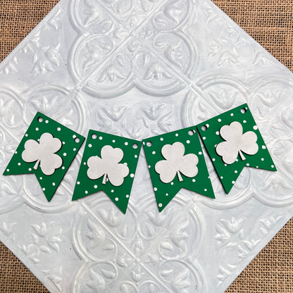 The Heartland Tiered Tray Garlands – Painted, featured here in a small banner with four green flags adorned with white shamrocks and polka dots, are displayed on a textured white background. Choose from 12 styles to suit your decor!.
