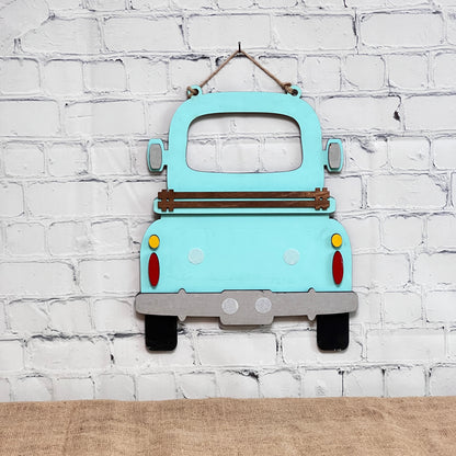 A light blue Antique Truck Interchangeable Base - Painted by Janet's Craft Corner hangs on a white brick wall above burlap. Seen from the back with wood accents and colorful tail lights, it's perfect for customizable décor.