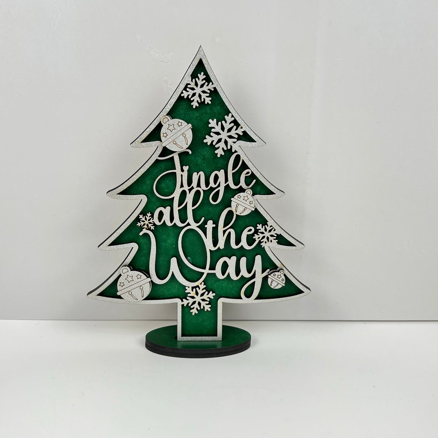 A captivating piece from Janet's Craft Corner, the Standing Christmas Tree Shelf Sitters are decorative wooden trees set against a green background. They beautifully feature the words "Jingle all the Way" in elegant white cursive, enhanced with charming snowflakes and ornaments. Mounted neatly on a small base, this delightful holiday decor is perfect for any shelf display.