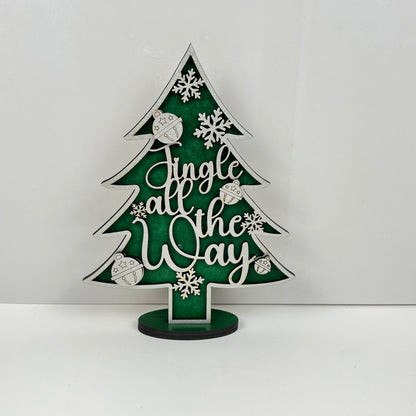 A captivating piece from Janet's Craft Corner, the Standing Christmas Tree Shelf Sitters are decorative wooden trees set against a green background. They beautifully feature the words "Jingle all the Way" in elegant white cursive, enhanced with charming snowflakes and ornaments. Mounted neatly on a small base, this delightful holiday decor is perfect for any shelf display.