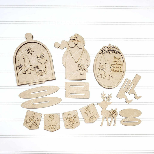 A flat lay of the unassembled "Oh Deer Decor Set" by Janet's Craft Corner is displayed on a white surface, showcasing wooden Christmas decorations that include a Santa, reindeer, trees, ornaments, and holiday message plaques. This DIY craft kit features festive cut-out designs perfect for interlocking or hanging as charming home décor pieces.