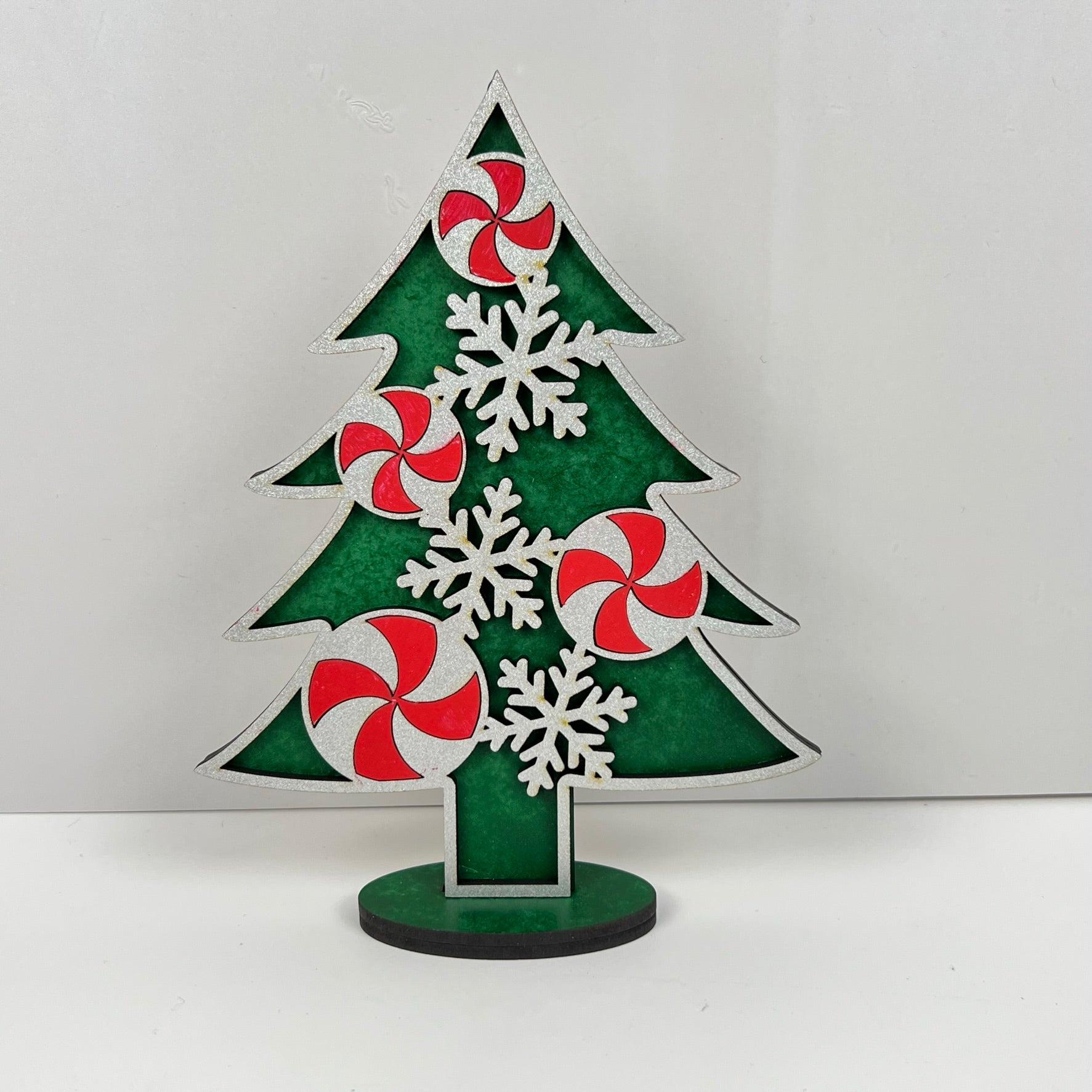 The Standing Christmas Tree Shelf Sitters from Janet's Craft Corner are perfect for holiday decor, showcasing green and white sections adorned with red and white peppermint swirl designs and white snowflakes. Ideal for shelf display, they stand on a black base against a plain white background.