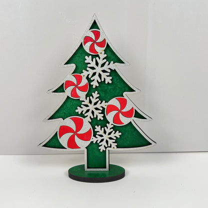 The Standing Christmas Tree Shelf Sitters from Janet's Craft Corner are perfect for holiday decor, showcasing green and white sections adorned with red and white peppermint swirl designs and white snowflakes. Ideal for shelf display, they stand on a black base against a plain white background.
