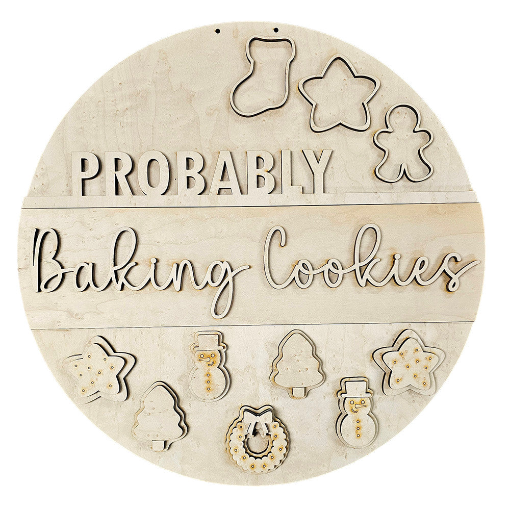 The "Probably Baking Cookies Door Hanger - DIY Home Decor Kit" by Janet's Craft Corner is a charming wooden sign featuring cutout letters and adorned with cookie cutter shapes like stockings, stars, gingerbread figures, snowmen, a tree, and a wreath for delightful personalized decor.