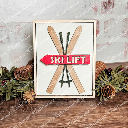 The Ski Lift Interchangeable Sign by Janet's Craft Corner is a DIY craft featuring hand-painted crossed skis, poles, and a red arrow pointing to "Ski Lift." Framed in wood with pinecones and greenery, it captures rustic charm for home decor.