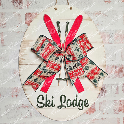 Janet's Craft Corner offers a rustic Ski Lodge Door Hanger with crossed red skis and ski poles, accented by a red and green bow. "Ski Lodge" is elegantly displayed on a textured background, enhancing home décor charm.