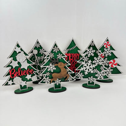 Janet's Craft Corner offers Standing Christmas Tree Shelf Sitters that are perfect for a shelf display. These decorative wooden trees feature words like "Believe," "Jingle," and "Merry" along with illustrations of snowflakes, ornaments, and candy. A reindeer silhouette adds to the festive holiday decor.