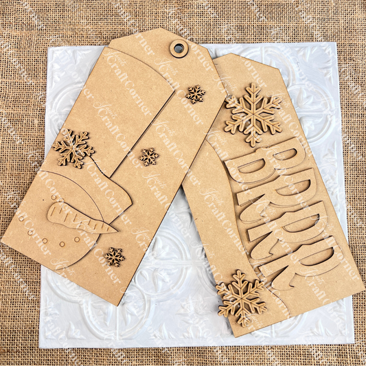 Two Winter Door Tags by Janet's Craft Corner: one says "BRRR" with snowflakes, the other shows a carrot and snowflakes—ideal for seasonal DIY home decor. Both brown kraft paper tags are shown on a white patterned tile background.