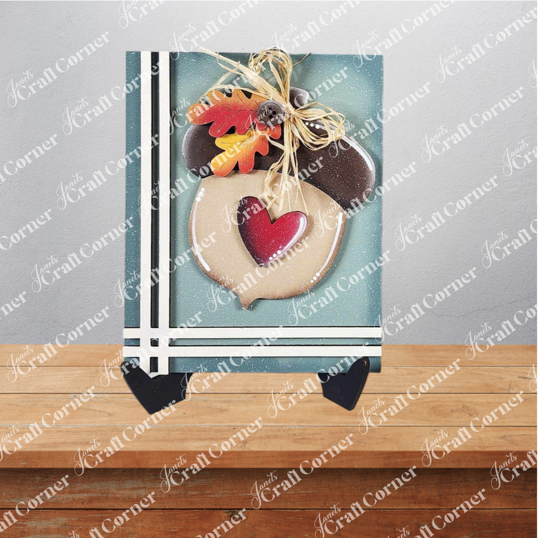 Janet's Craft Corner Fall Switchable Farmhouse Sign is a DIY seasonal decor kit featuring an acorn-shaped wooden plaque with heart cutout, faux autumn leaves, and raffia bow—perfect for charming fall displays on any tabletop.
