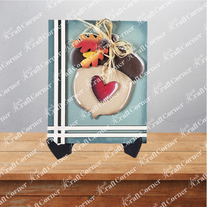 Janet's Craft Corner Fall Switchable Farmhouse Sign is a DIY seasonal decor kit featuring an acorn-shaped wooden plaque with heart cutout, faux autumn leaves, and raffia bow—perfect for charming fall displays on any tabletop.
