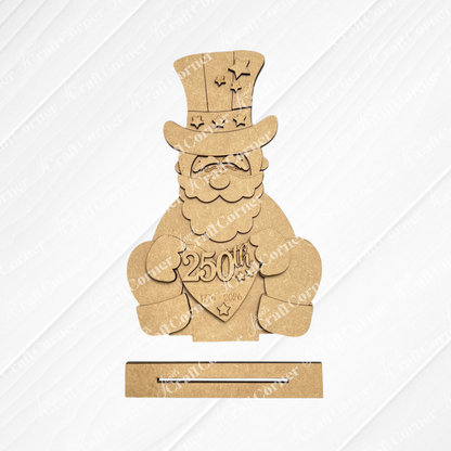 Janet's Craft Corner America 250 Mini Shelf Sitters DIY craft kit features a laser-cut unfinished wood smiling man with top hat holding a "250th" and "1873-2023" heart. Comes with rectangular base—perfect for patriotic tiered tray displays.