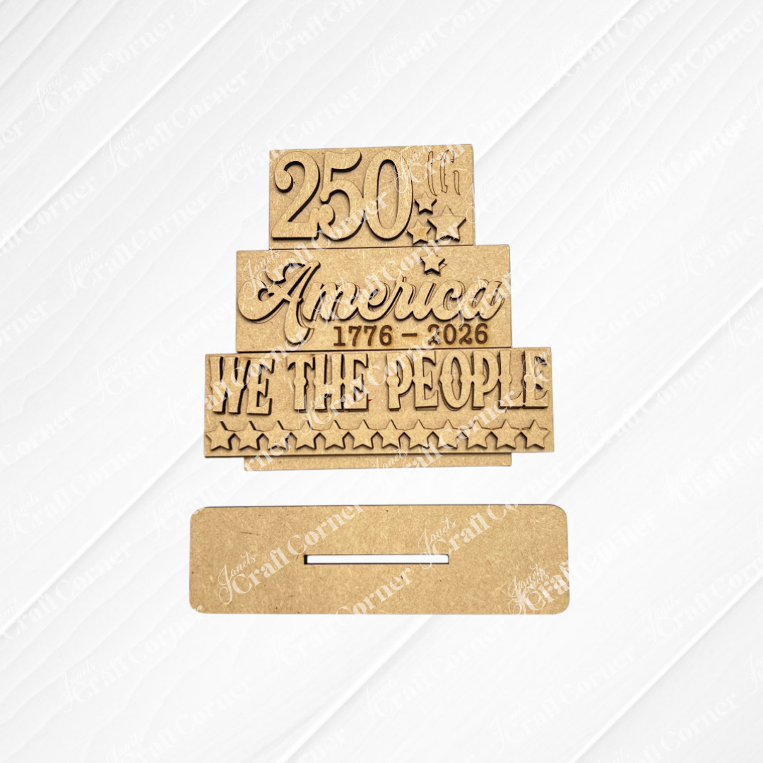 Janet's Craft Corner’s America 250 Mini Shelf Sitters kit features unfinished wood cut-outs reading "250th," "America 1776-2026," and "WE THE PEOPLE" with stars, plus a slotted base for easy tiered tray or shelf display.