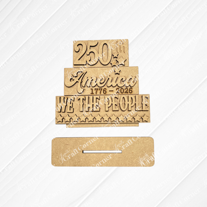 Janet's Craft Corner’s America 250 Mini Shelf Sitters kit features unfinished wood cut-outs reading "250th," "America 1776-2026," and "WE THE PEOPLE" with stars, plus a slotted base for easy tiered tray or shelf display.
