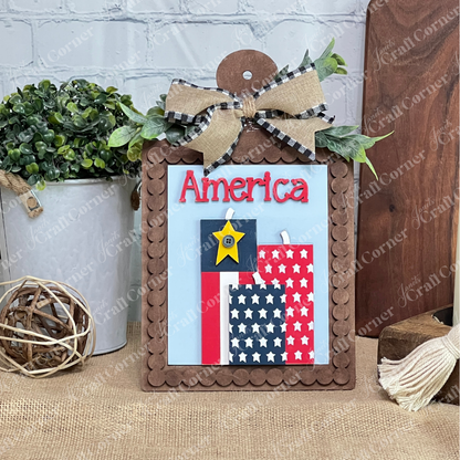 Janet's Craft Corner Patriotic Farmhouse Signs DIY craft kit features a wooden sign with “America” in red, gingham and burlap bow, star blocks, greenery, and rustic accents—perfect for tiered tray decor. Set of 1.