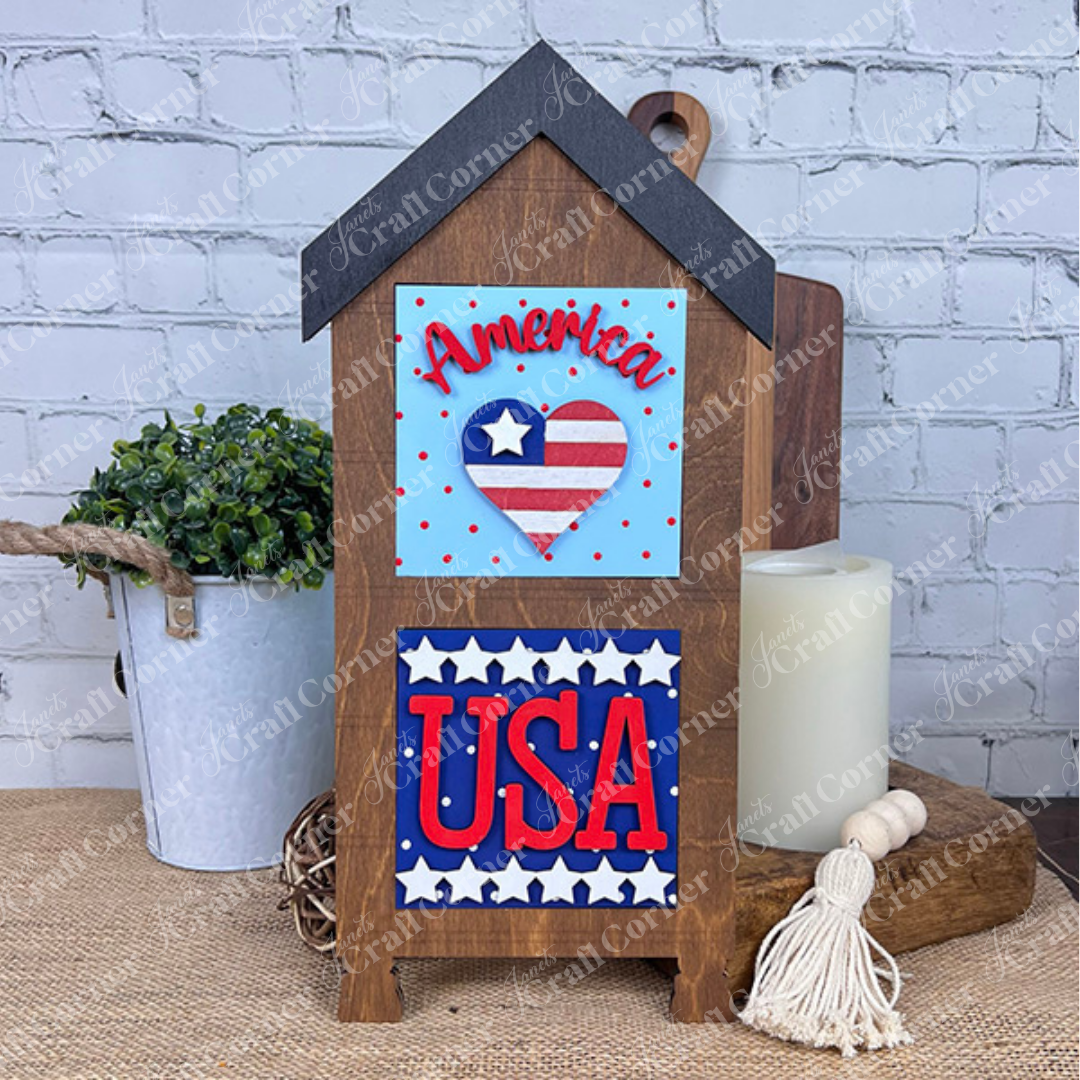 Janet's Craft Corner’s Patriotic Squares DIY craft kit features a wooden house-shaped décor piece with "America," a heart of stars and stripes, and bold red "USA"—perfect for Independence Day or seasonal home decorating.
