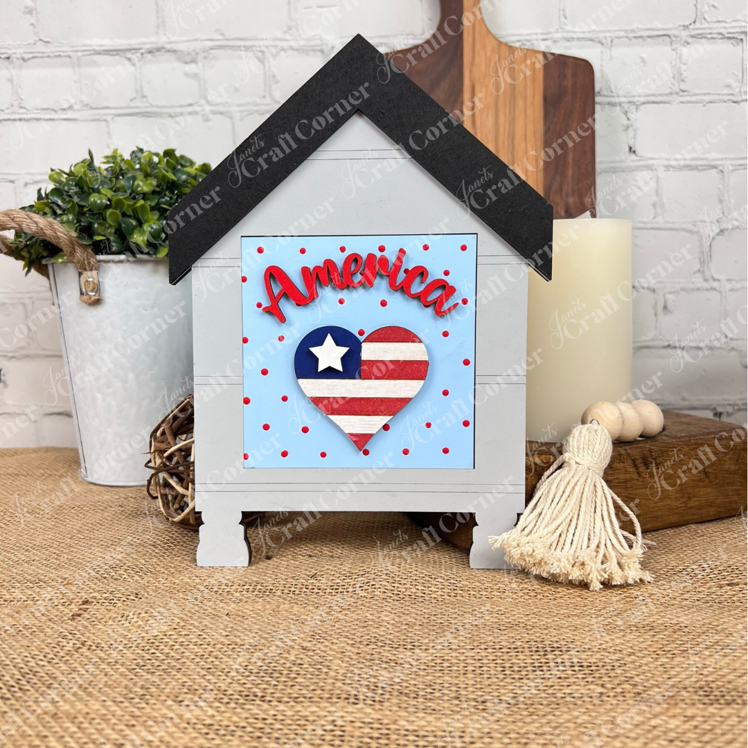 The Patriotic Squares DIY craft kit from Janet's Craft Corner features a house-shaped wooden sign with a heart in an American flag design, red polka dots, and "America" script—perfect for Independence Day décor on tables or with farmhouse accents.